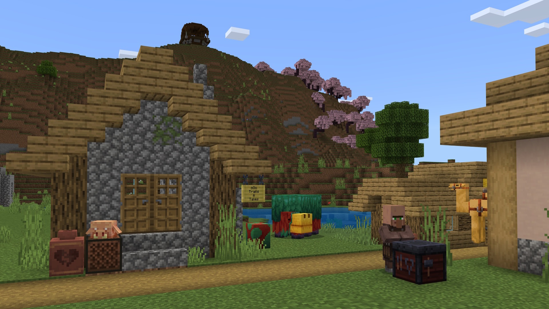 A Minecraft screenshot featuring a village, villager, sniffer, with a cherry grove and pillager outpost on the side of a mountain in the background.